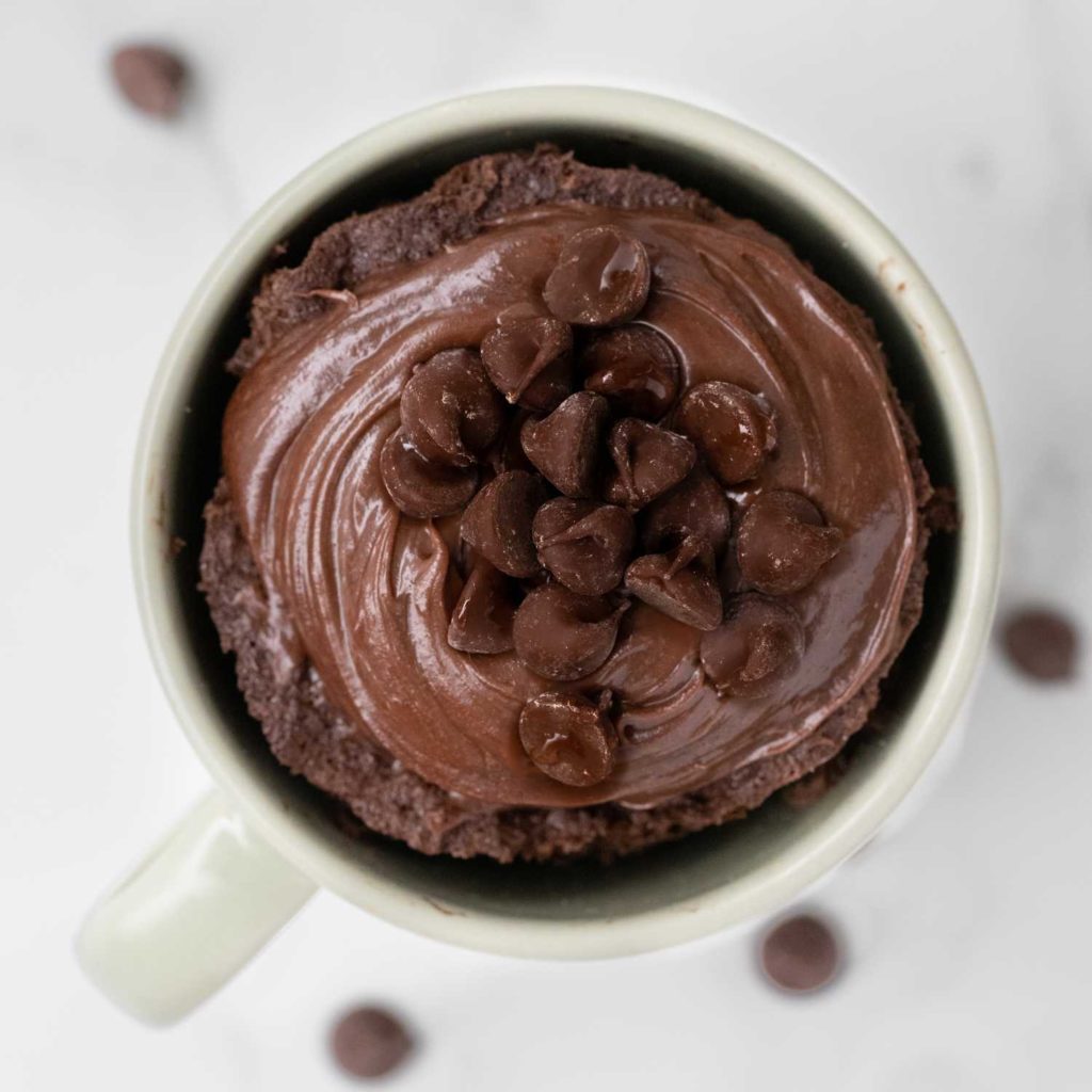 Gooey chocolate mug cake with chocolate frosting and chocolate chips on top.