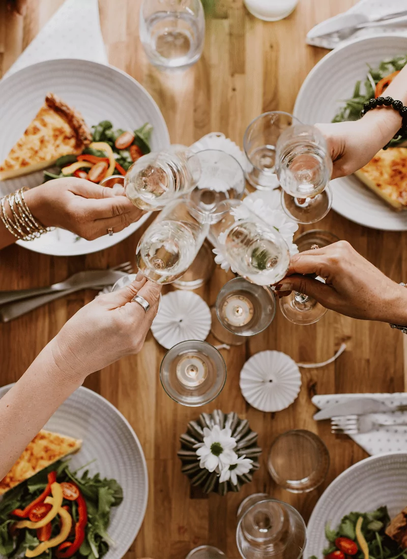 Hands clinking glasses over a meal table for wedding rehearsal dinner ideas on a budget
