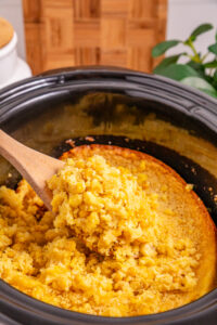 Wooden spoon in a slower cooker dipping out corn casserole